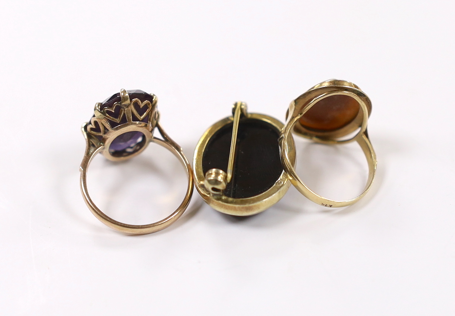 A 14k and oval cameo shell set ring, a 14k and synthetic colour change corundum set ring and a yellow metal and black onyx set brooch.